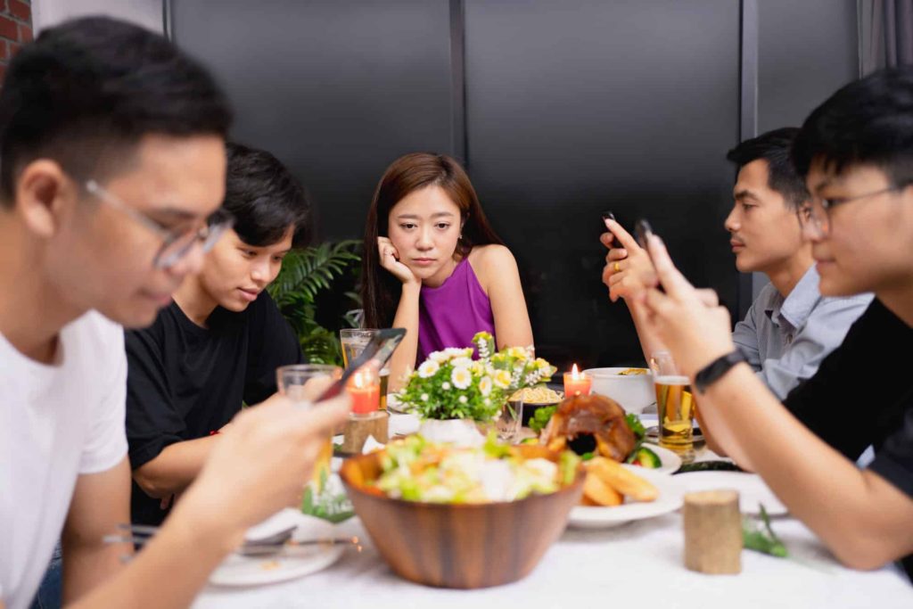 Family on a dinner table filled with food, one woman looks sad, everyone else are on their phones.