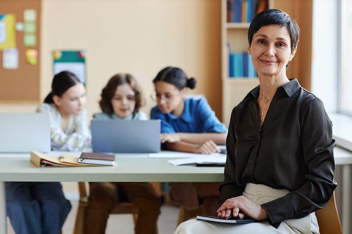 Portrait of teacher looking at camera sitting at lesson with children in background