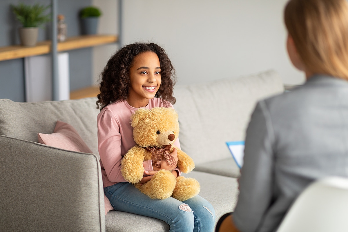 Image of a child holding a teddy bear in front of a psychotherapist