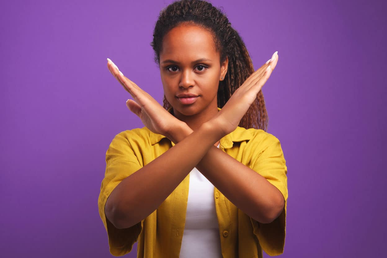 Woman with her hands crossed in "no" gesture, on a purple background.