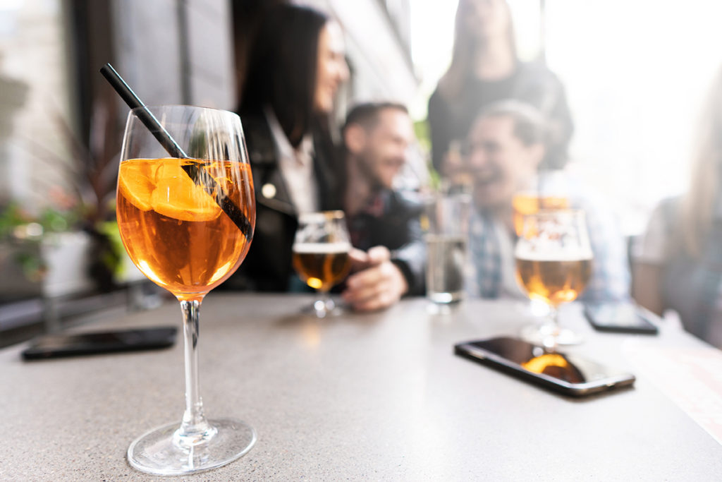 Aperol Spritz cocktail on a table with a sitting group of friends on background